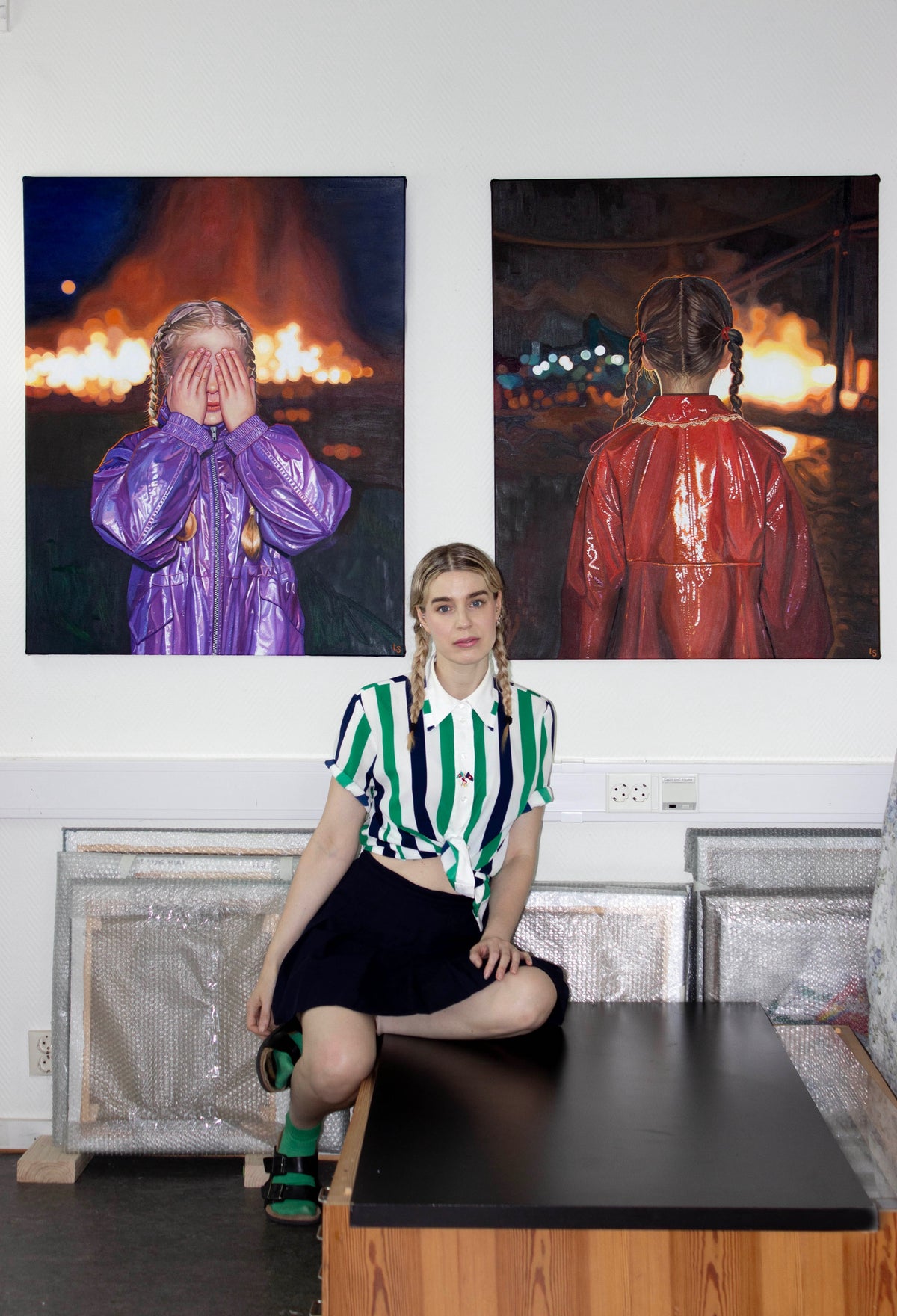 Lovisa Sköld in front of two oil paintings of figures in glossy coats before a fire