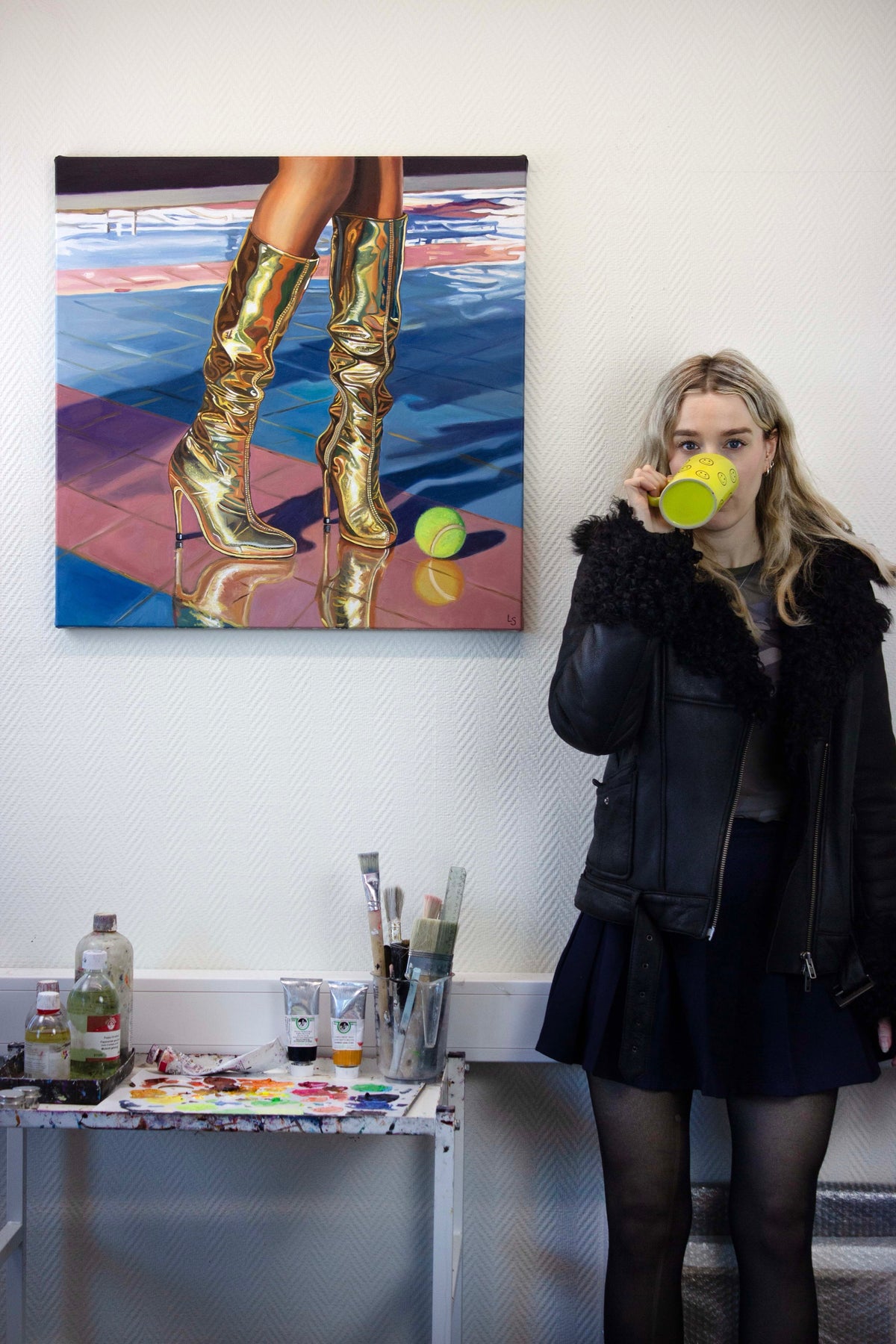 Lovisa Sköld beside her oil painting of gold boots and a tennis ball by a pool